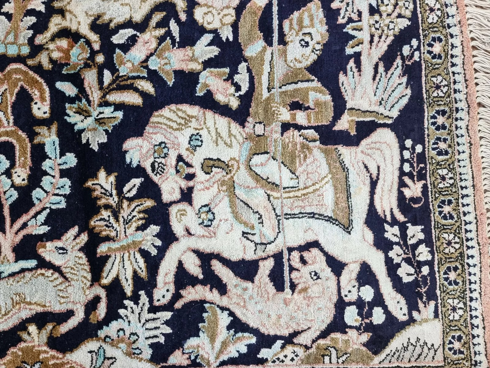 Close-up of the intricate hunting motifs on a handmade Qum silk rug from the 1970s

