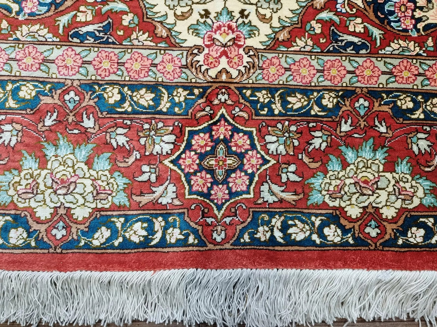 Persian silk rug featuring vibrant red and cream tones with blue floral accents.
