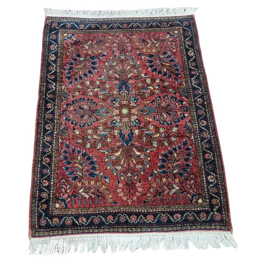 Handmade antique Persian Sarouk rug with a deep red base and intricate floral motifs
