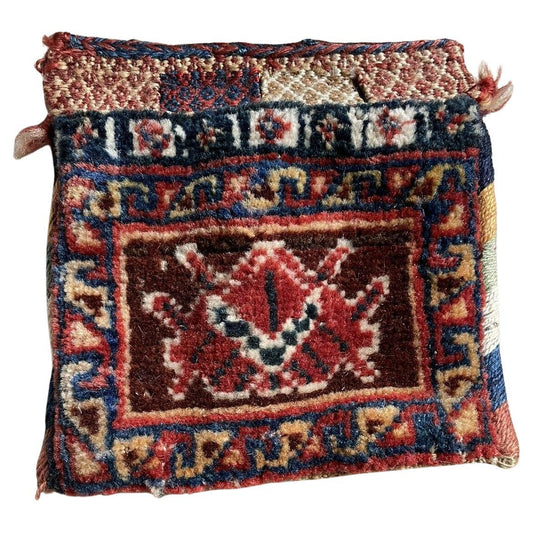 Close-up view of a handmade antique Persian Gashkai small bag (1900s) showcasing intricate geometric and floral patterns in red, blue, cream, and yellow.