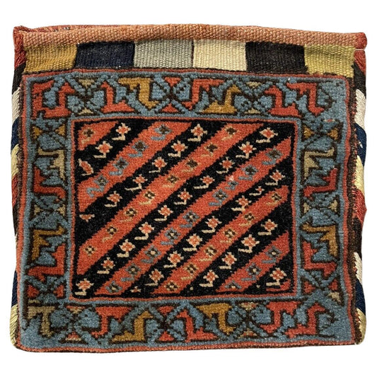 Close-up view of a handmade antique Persian Gashkai small bag (1900s) in an unusually large size (9" x 9" or 24cm x 24cm). It features intricate geometric and floral patterns in earthy tones of blue, brown, and neutral hues, reflecting the natural colors of its Persian origin.