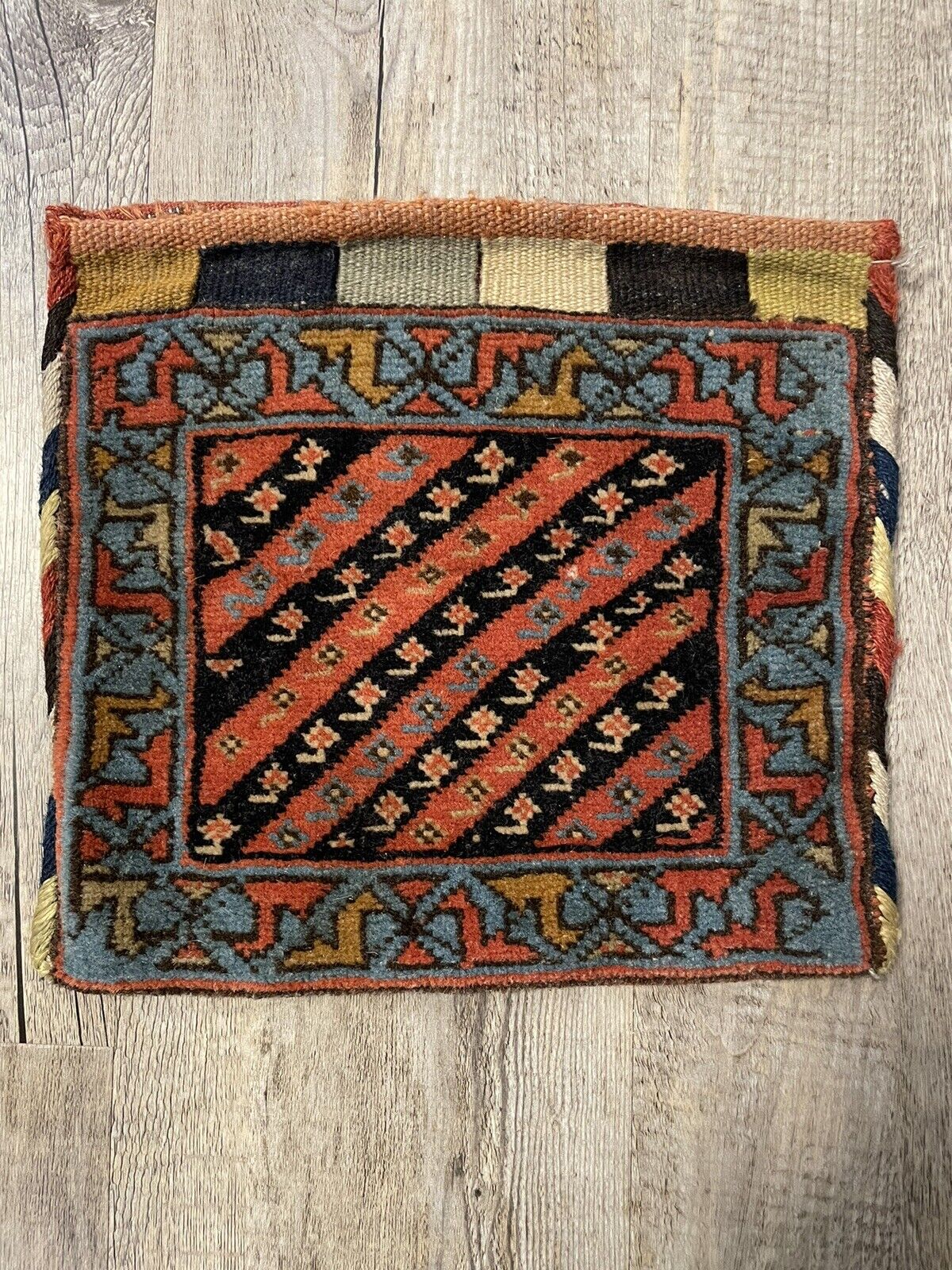 The handmade antique Persian Gashkai small bag (1900s) held in hand, showcasing its unusually large size (9" x 9") and versatility as a unique accessory.