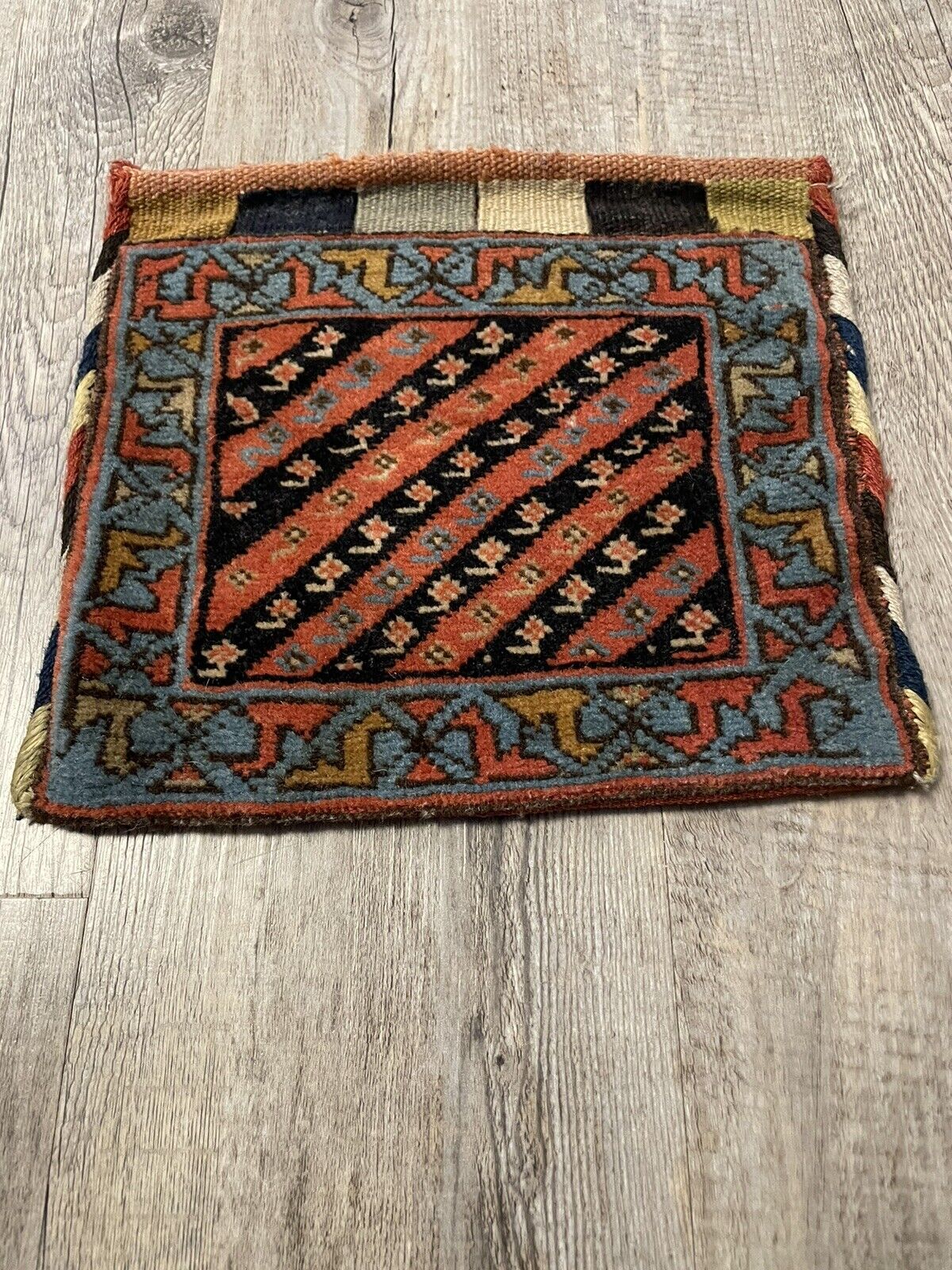 The handmade antique Persian Gashkai small bag (1900s) displayed on a shelf with other collectible items, emphasizing its value as a cultural artifact.