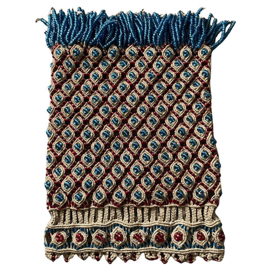Close-up view of a handmade vintage Malian bag (1960s) crafted from crocheted cotton fabric in a rich, natural color. The bag features traditional Malian beadwork with diamond shapes (a symbol of wisdom and wealth in African art) in vibrant colors. A playful fringe of blue beads dances along the top edge, adding movement and visual interest.