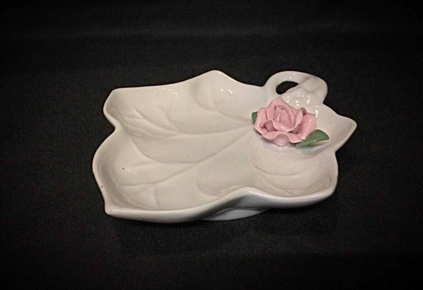 Delicate ceramic rose paperweight showcasing intricate craftsmanship on a small dish.
