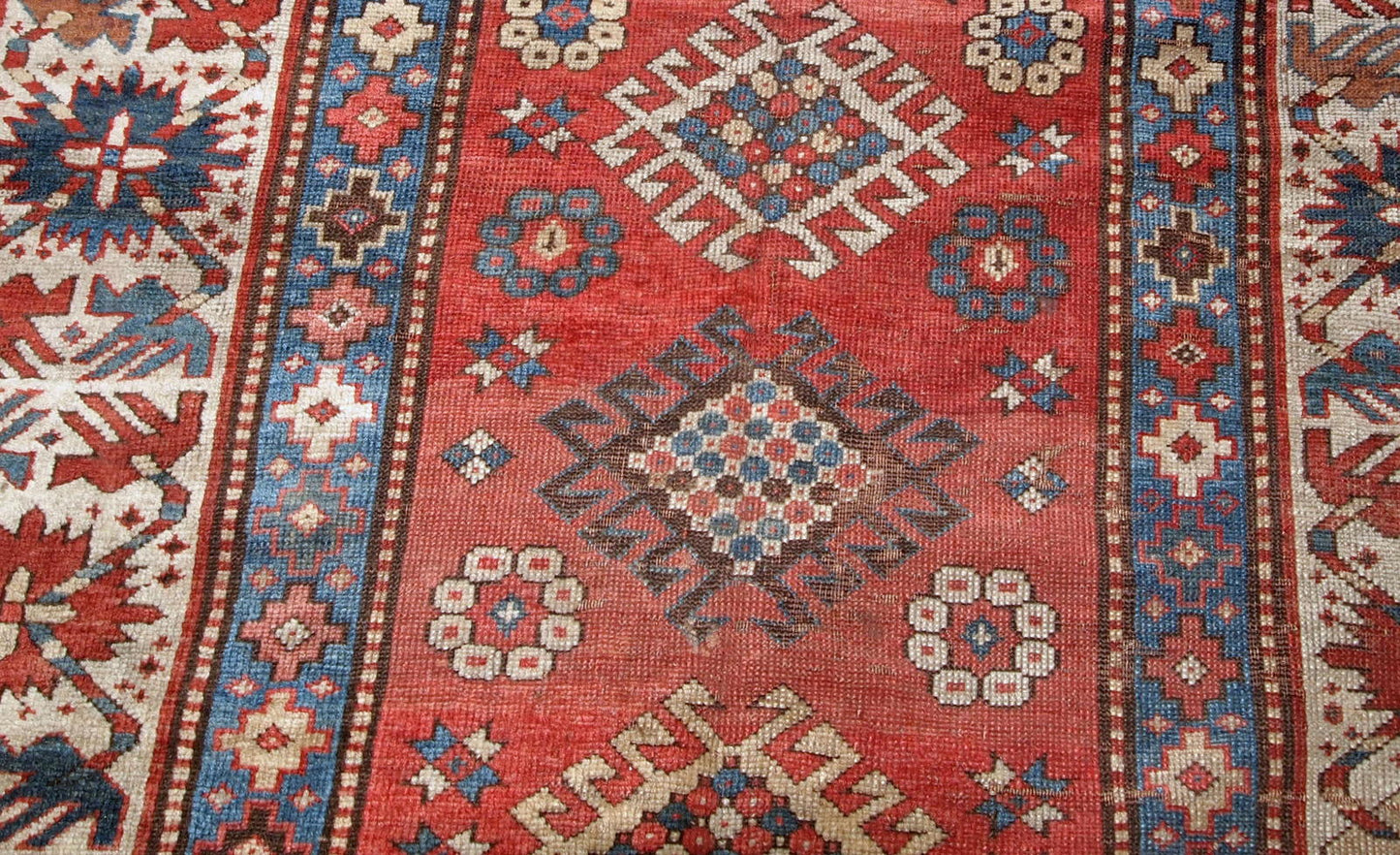 Handmade antique Caucasian Kazak rug in red and beige shades. The rug is from the end of 19th century in original condition, it has some low pile, a little cut on one side.