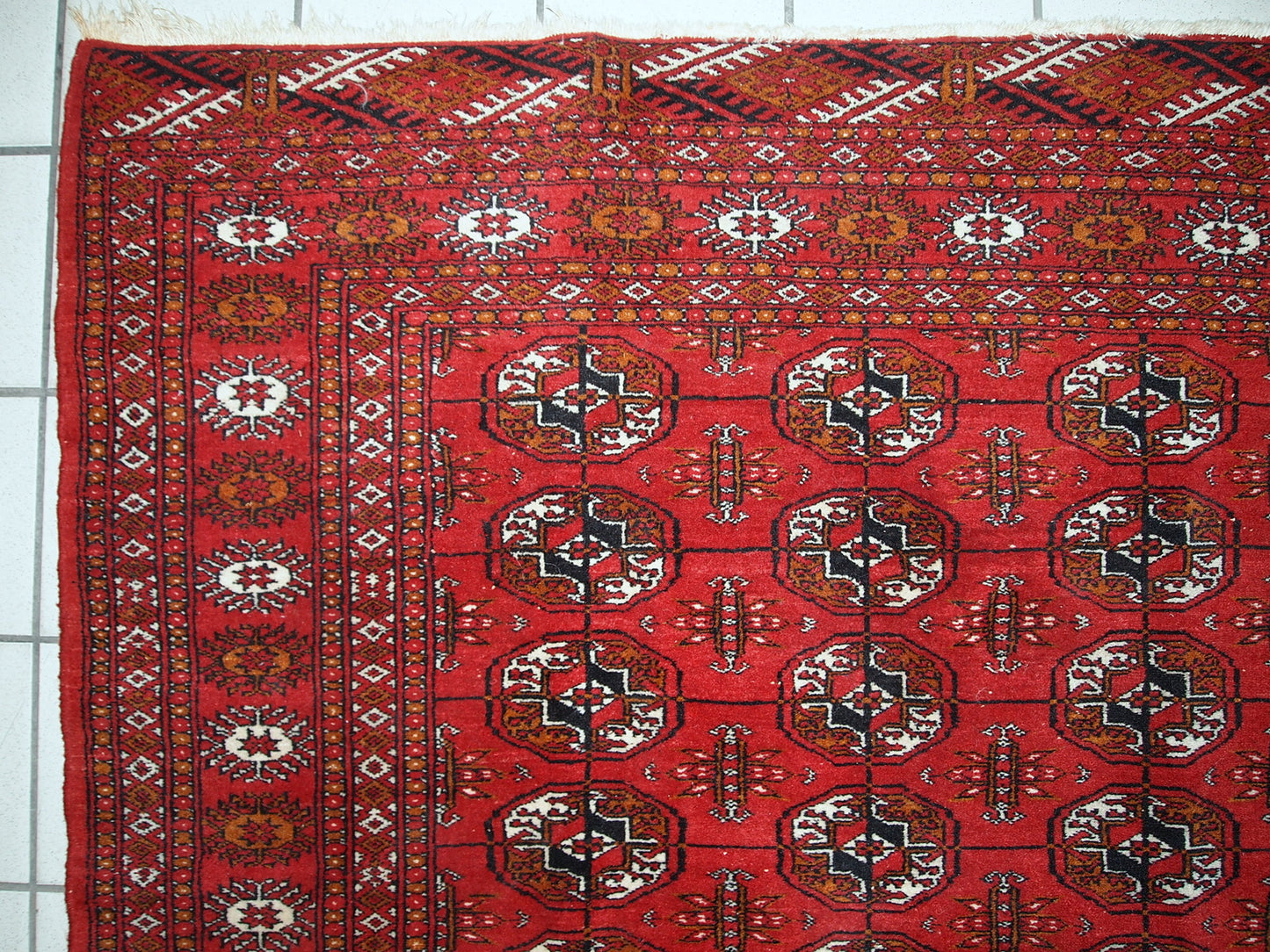 Handmade mid-century Pakistani rug in the style of Turkmen Tekke. Repeating elephant foot design on the bright red background. The rug has some signs of age but generally in original good condition.