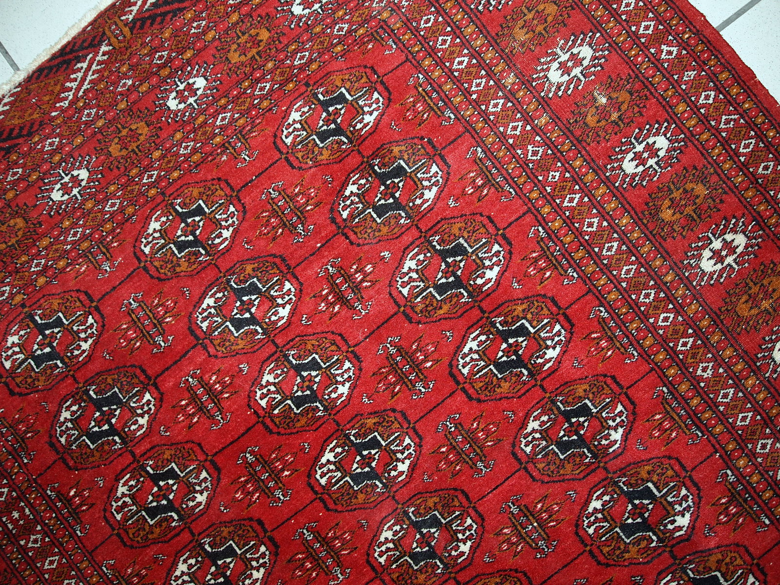 Handmade mid-century Pakistani rug in the style of Turkmen Tekke. Repeating elephant foot design on the bright red background. The rug has some signs of age but generally in original good condition.