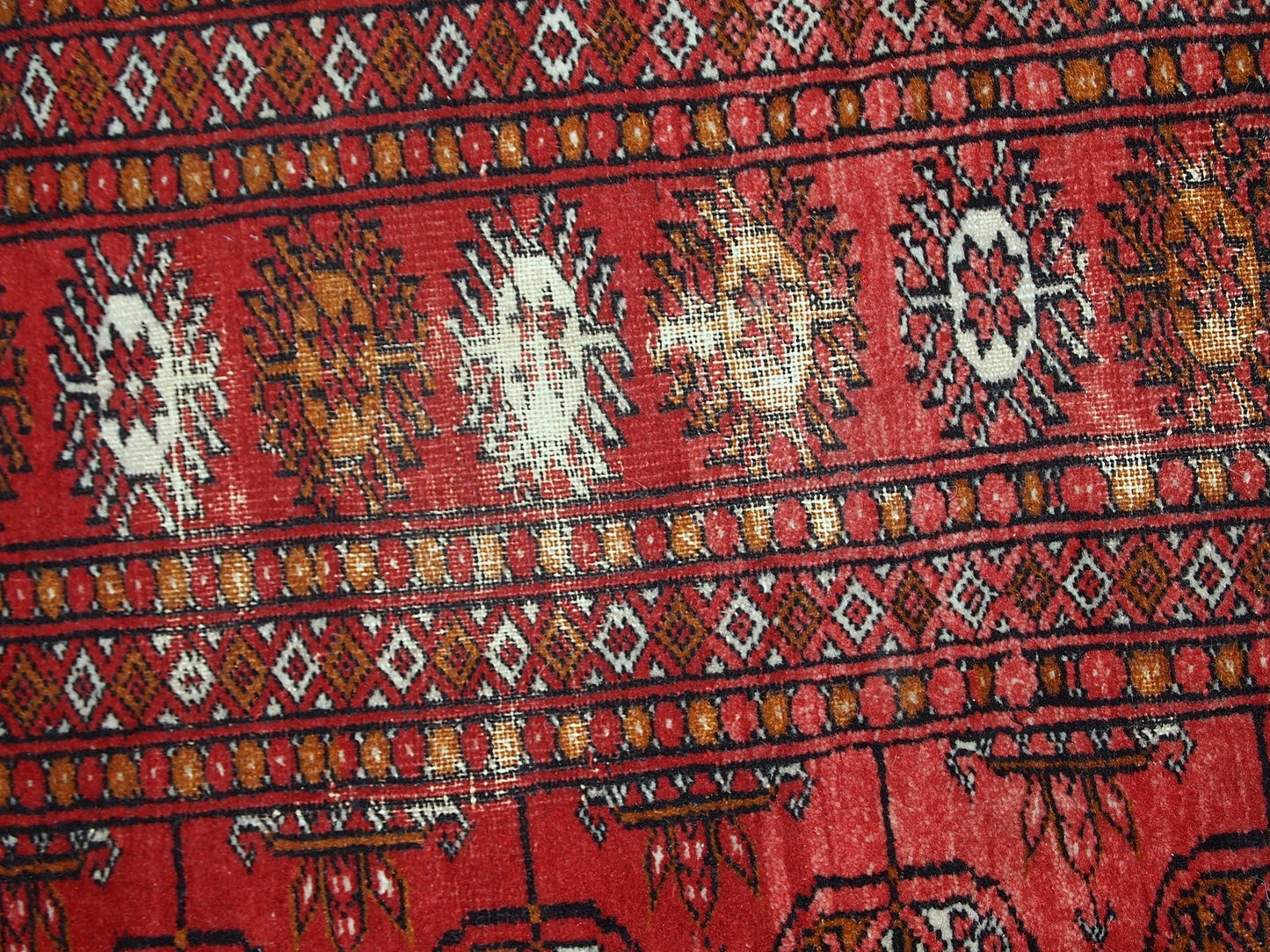 Handmade mid-century Pakistani rug in the style of Turkmen Tekke. Repeating elephant foot design on the bright red background. The rug has some signs of age but generally in original good condition.