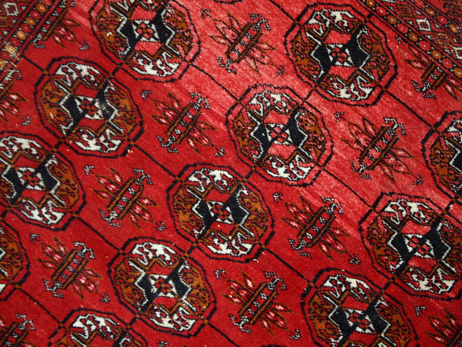 Handmade mid-century Pakistani rug in the style of Turkmen Tekke. Repeating elephant foot design on the bright red background. The rug has some signs of age but generally in original good condition.