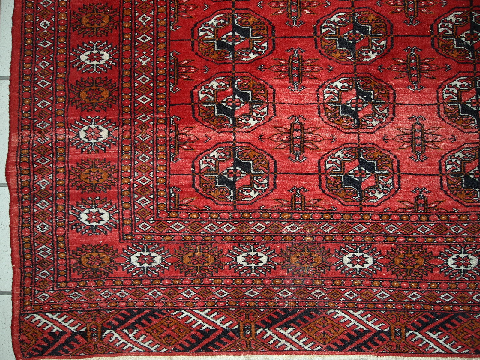 Handmade mid-century Pakistani rug in the style of Turkmen Tekke. Repeating elephant foot design on the bright red background. The rug has some signs of age but generally in original good condition.